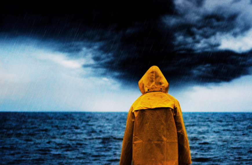 Eine Person in einem gelben Regenmantel steht bei Unwetter im Meer.
